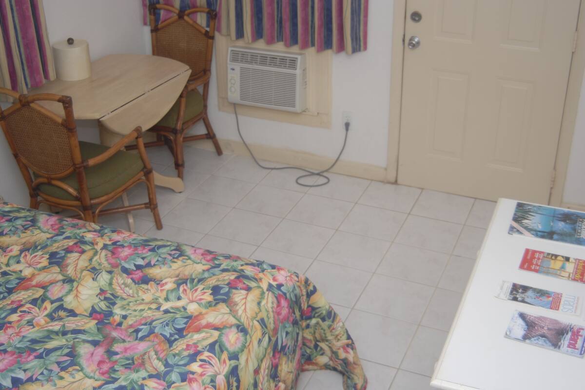 Quarto com cama, mesa, cadeiras, ar condicionado e porta.