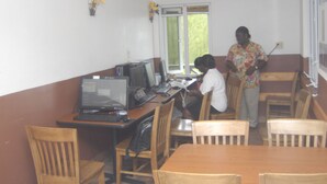 A room with a wooden table, chairs, and two desks with computers.