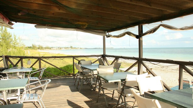An outdoor deck with tables and chairs overlooking a beach.