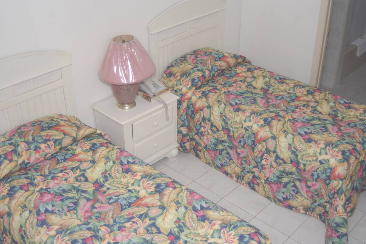 Quarto com duas camas, uma mesa de cabeceira com abajur e um telefone.