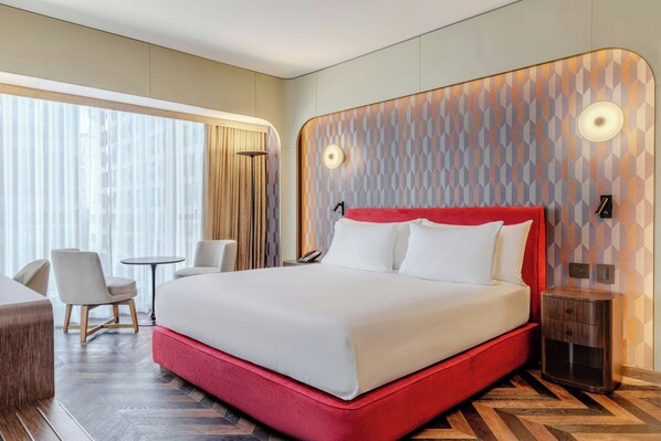A modern hotel room with a large bed, a desk, and a chair.