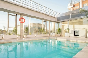 A rooftop swimming pool with a lifebuoy, potted plants, and a view of buildings.