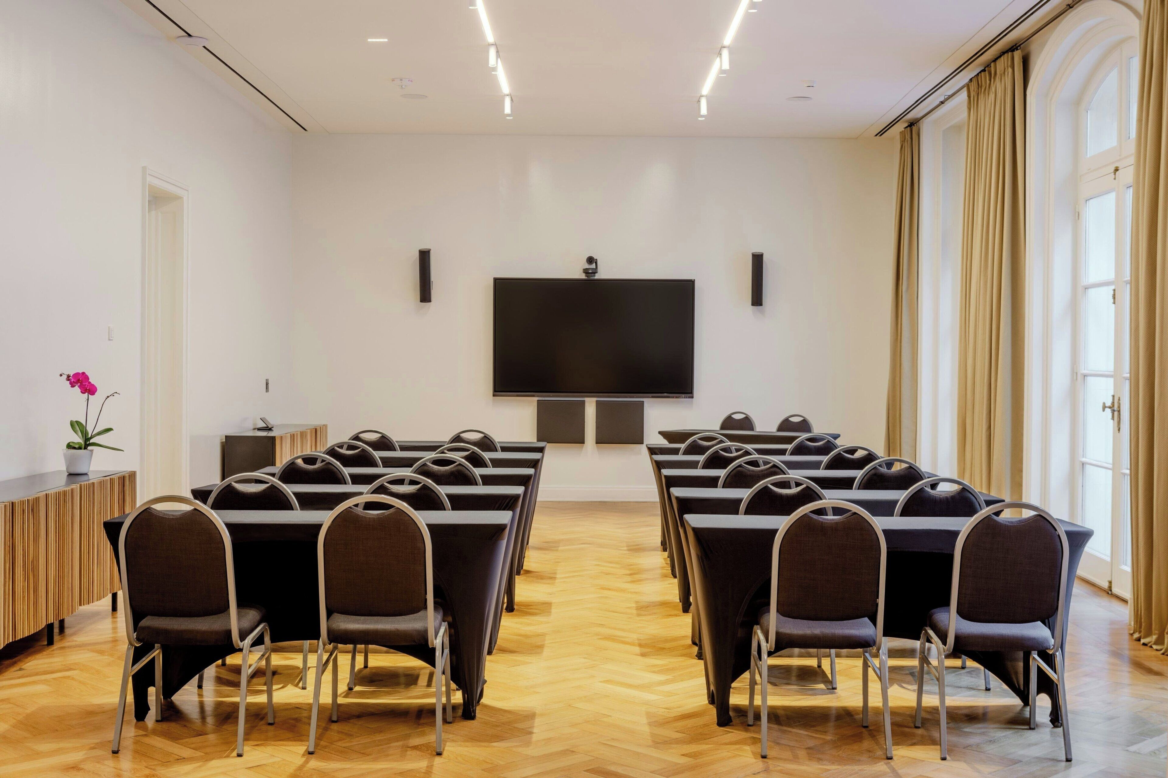 A conference room with a large table, chairs, a flat-screen TV, and a potted plant.