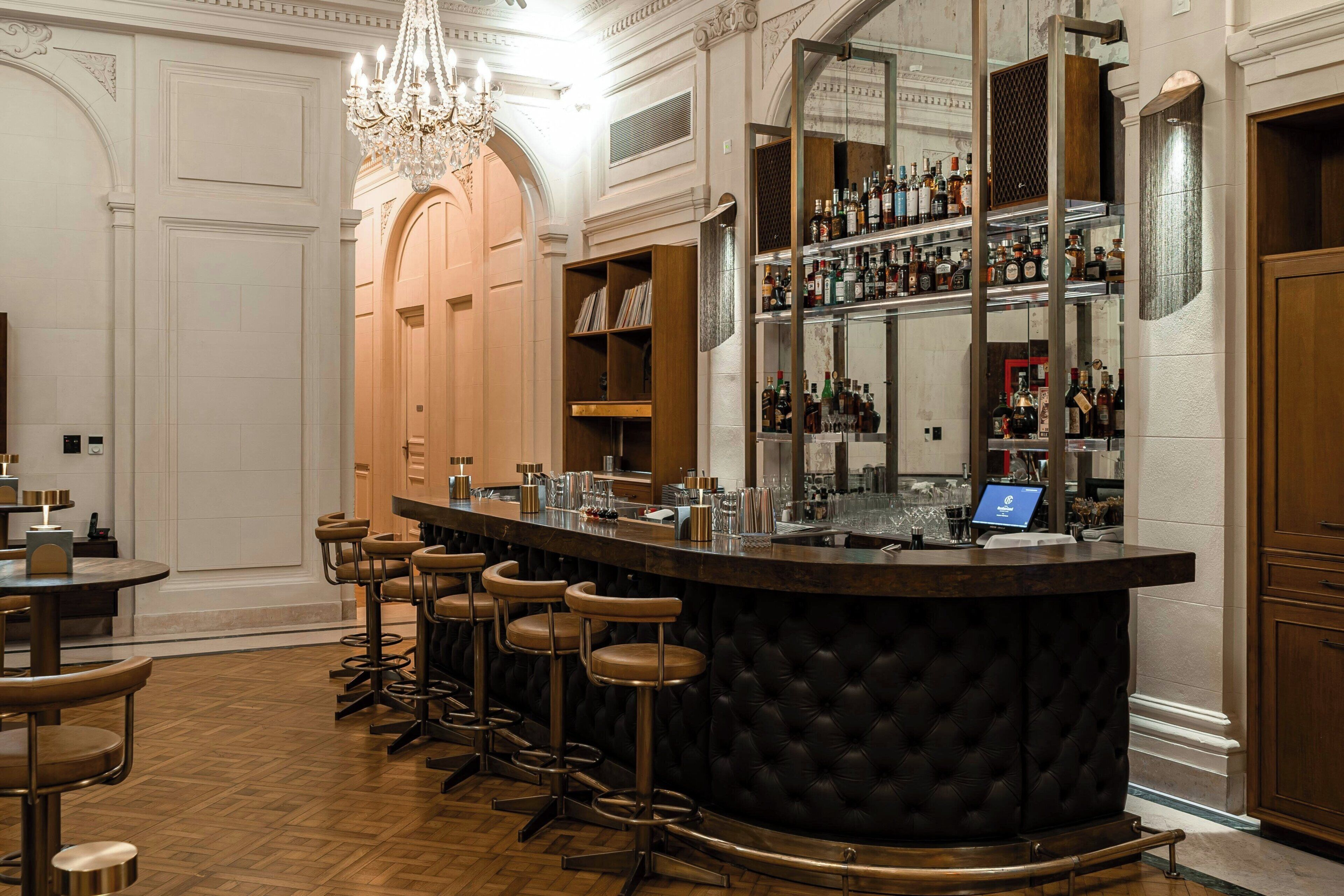 Un espace bar doté d’un comptoir sombre, de plusieurs tabourets et d’une variété de bouteilles et de verres.