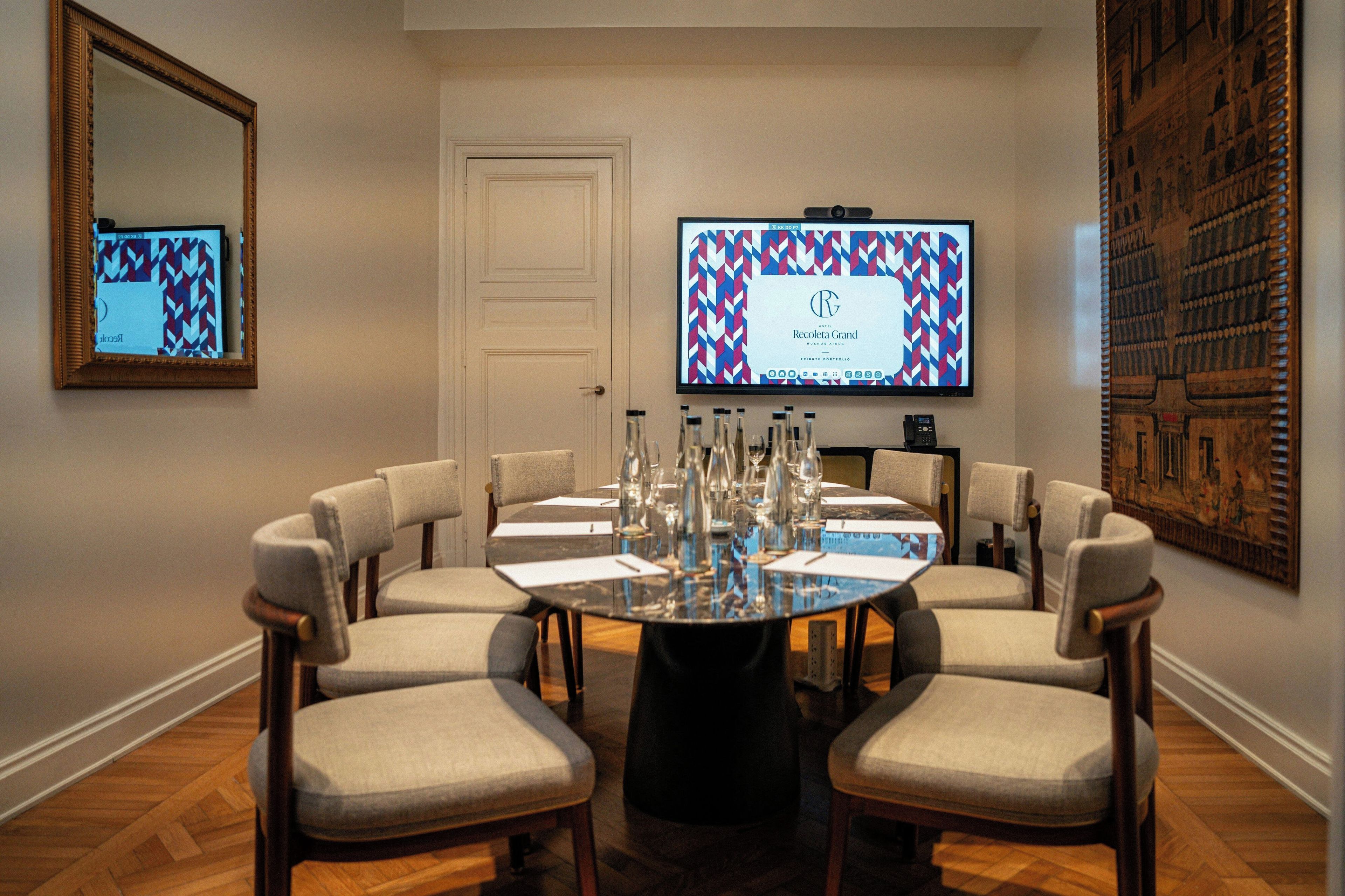 Une salle de conférence avec une table ronde, six chaises, un écran de télévision et une porte.