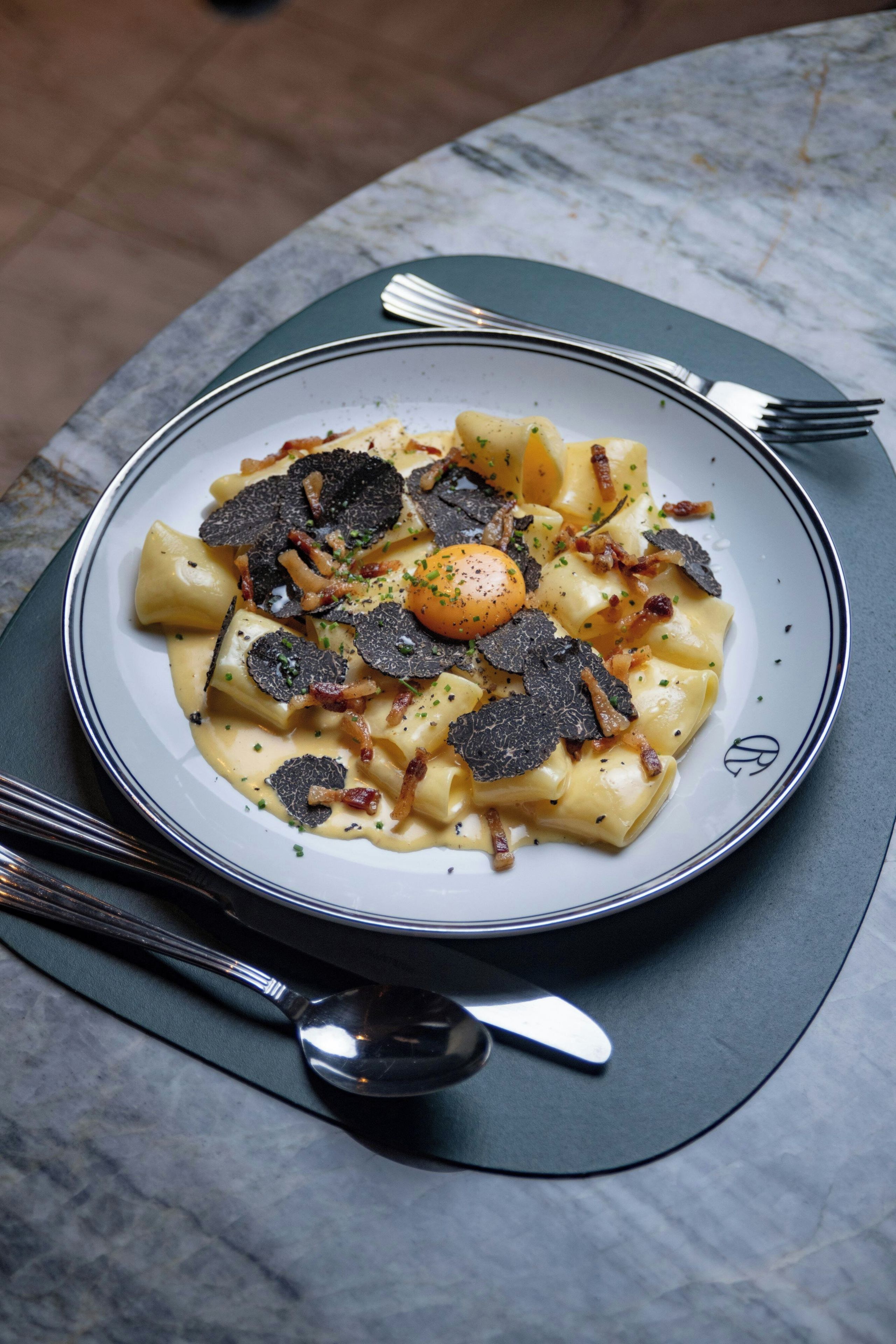 Un piatto di pasta con tartufo nero e pancetta su un tavolo in marmo.