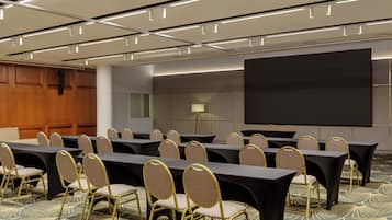 Un salón de conferencias con varias mesas y sillas, una pantalla grande y piso alfombrado.