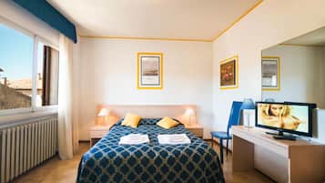Ein Hotelzimmer mit einem Bett, zwei Nachttischen, einem Schreibtisch mit Stuhl, einem Fernseher und einem Fenster mit Aussicht.