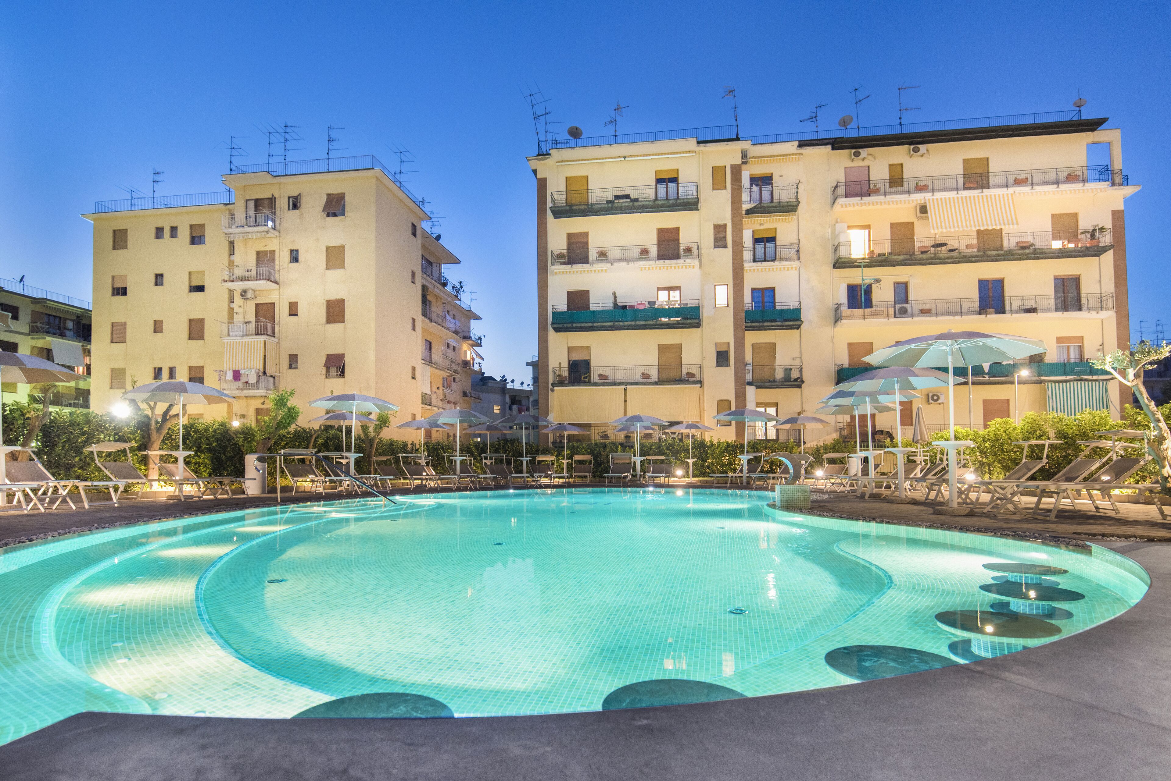 Une piscine entourée de bâtiments à plusieurs étages dotés de balcons, avec des chaises longues et des parasols à proximité.