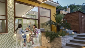 An outdoor bar area with two white bar stools, a large window, and a staircase leading to a wooden deck. - Hotel Leone (Sorrento)