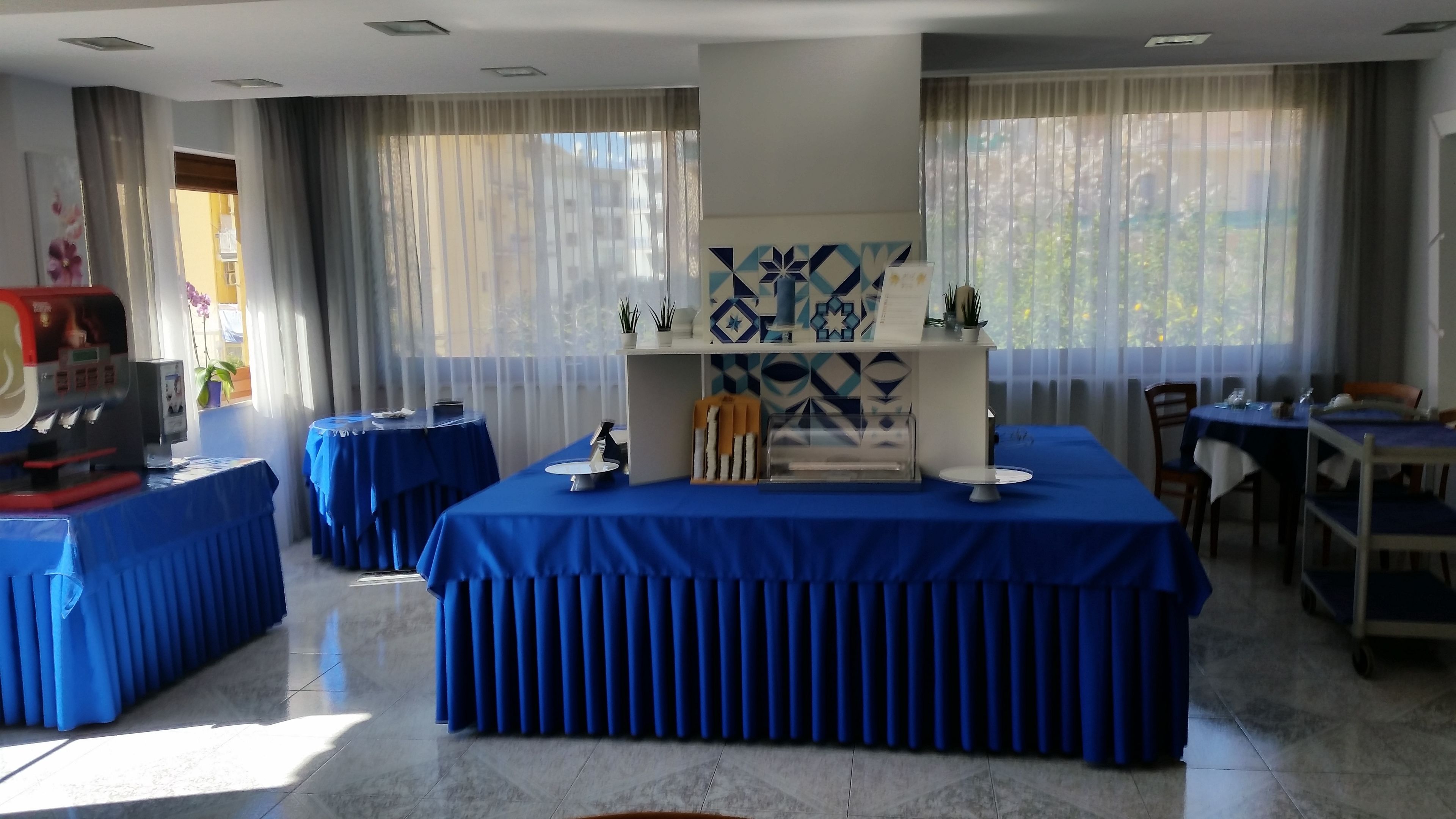 A hotel dining area with blue-covered tables, a coffee machine, and decorative items on a central display.
