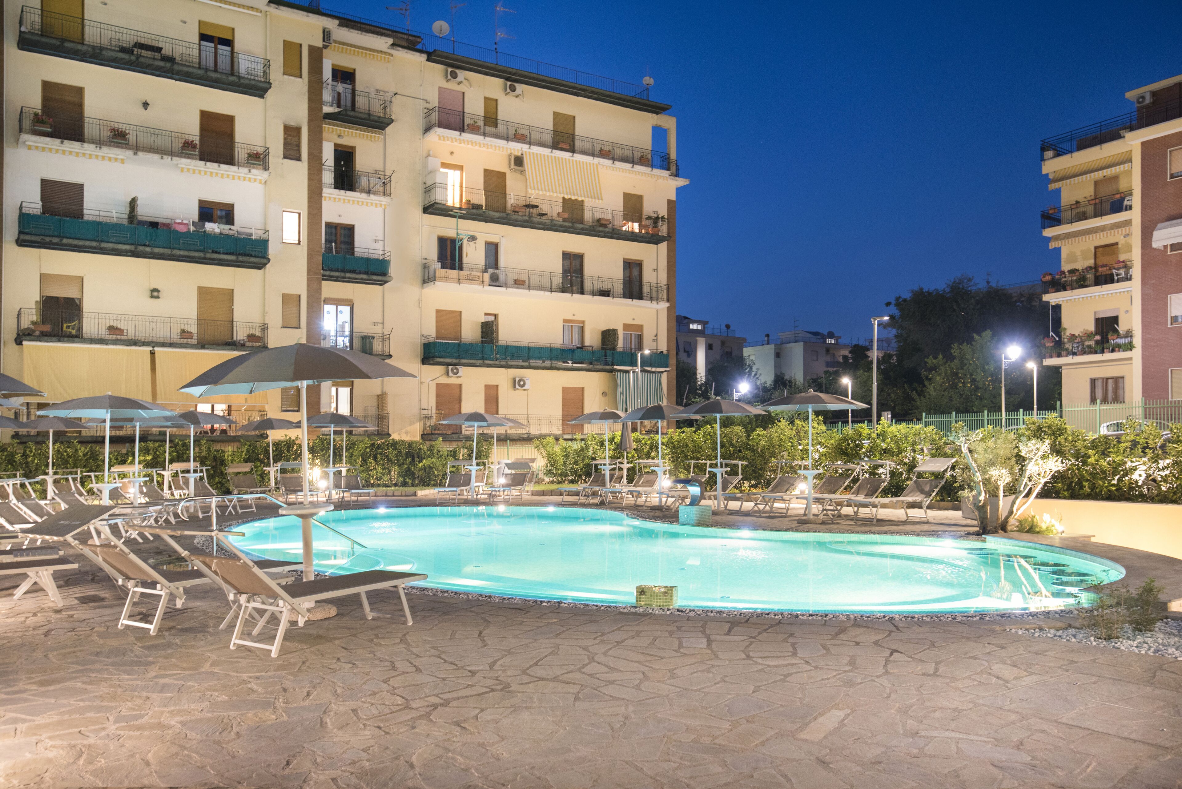 A swimming pool with lounge chairs and umbrellas, surrounded by multi-story buildings with balconies.