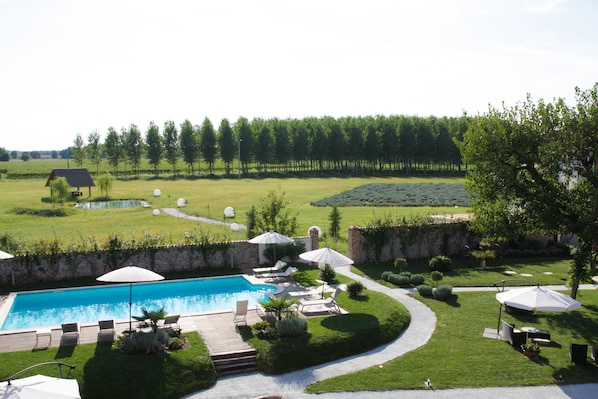 A swimming pool with lounge chairs and umbrellas, surrounded by a well-maintained lawn and trees.