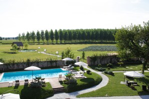 A swimming pool with lounge chairs and umbrellas, surrounded by a well-maintained lawn and trees.