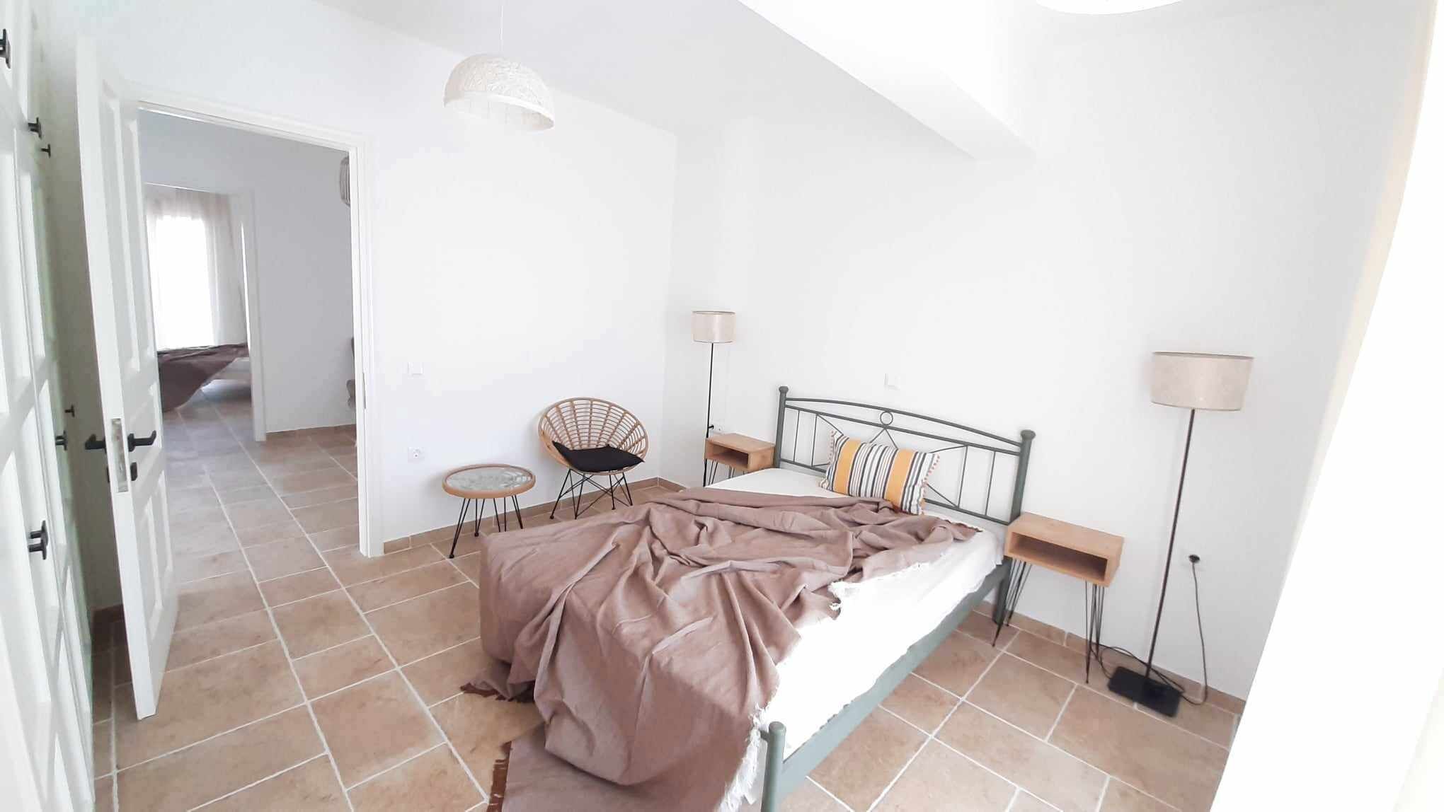 A bedroom with a bed, a chair, a lamp, and a floor lamp.
