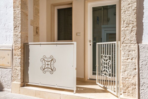 A building entrance with a metal gate, a door with a glass panel, and a small window above the door. - Dimora Grottone (Polignano a Mare)