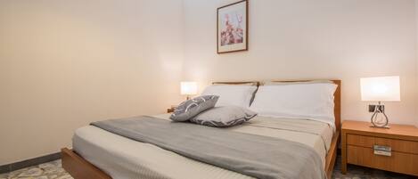 Un dormitorio con una cama, mesitas de noche, un cuadro colgado en la pared y un suelo con diseño de piedra.