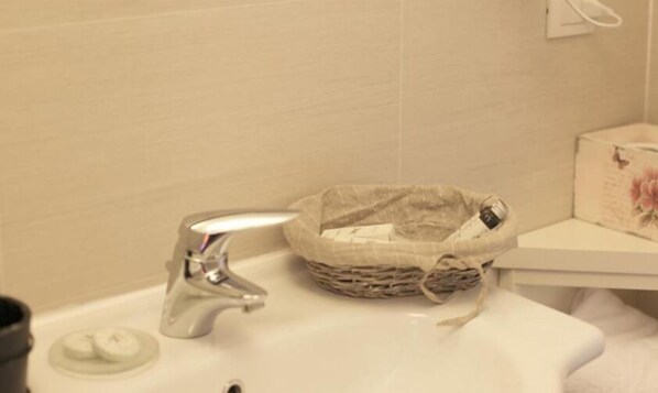 Un lavabo de baño con un grifo plateado, un jabonera y una cesta decorativa con una caja floral a un lado.