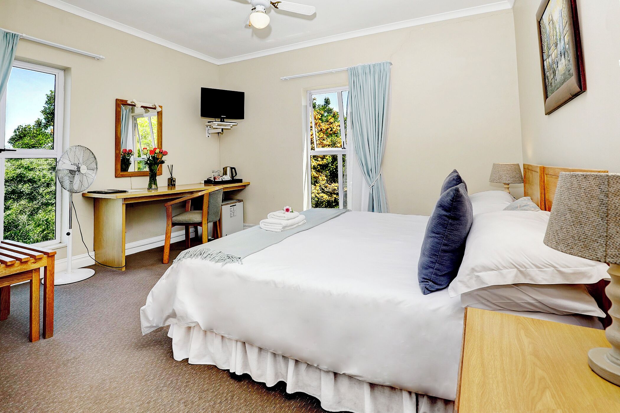 A bedroom with a bed, desk, chair, and a TV on the wall.
