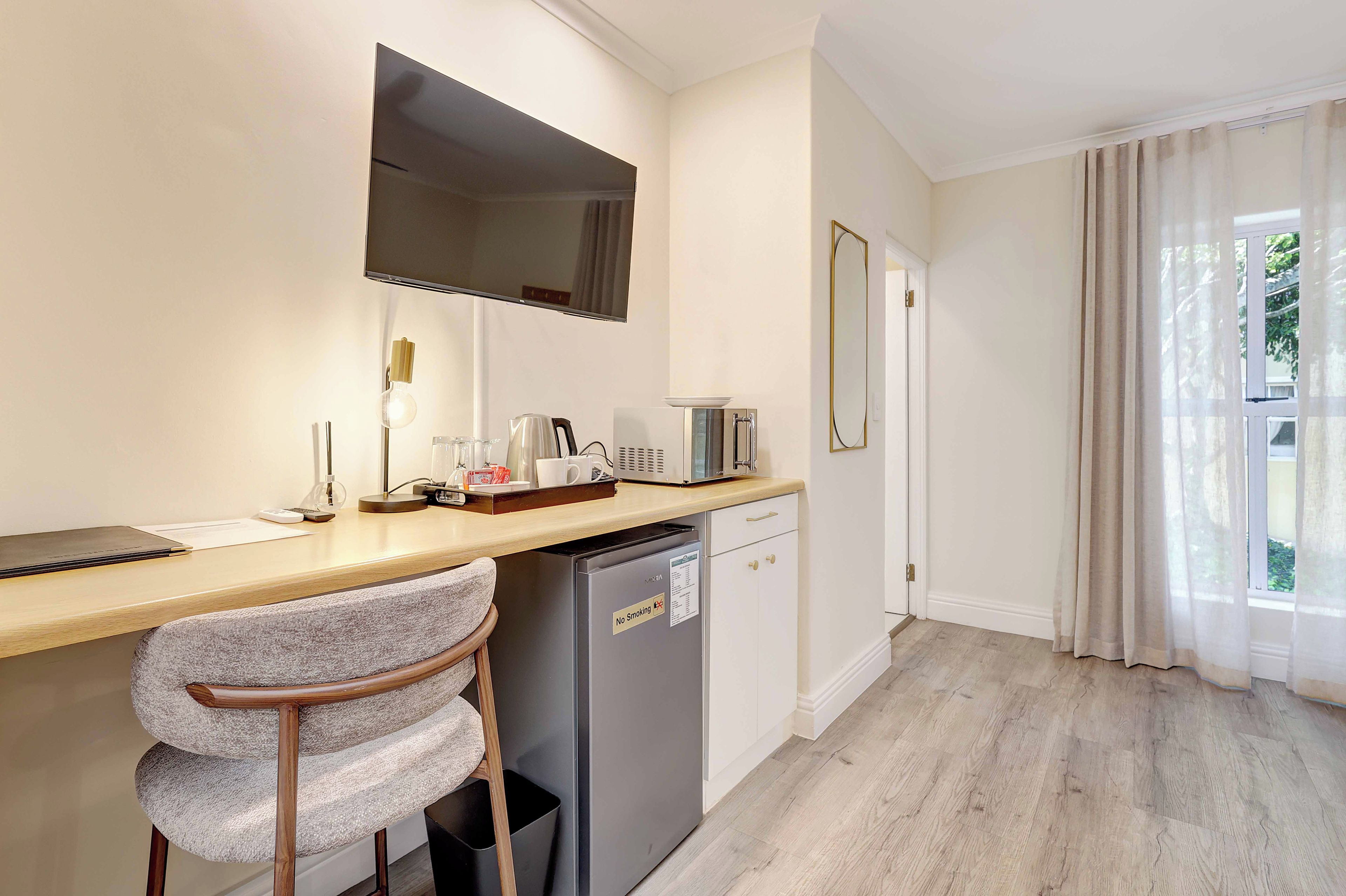 A compact kitchen with a refrigerator, microwave, and coffee maker. There are two chairs and a small table with a lamp.