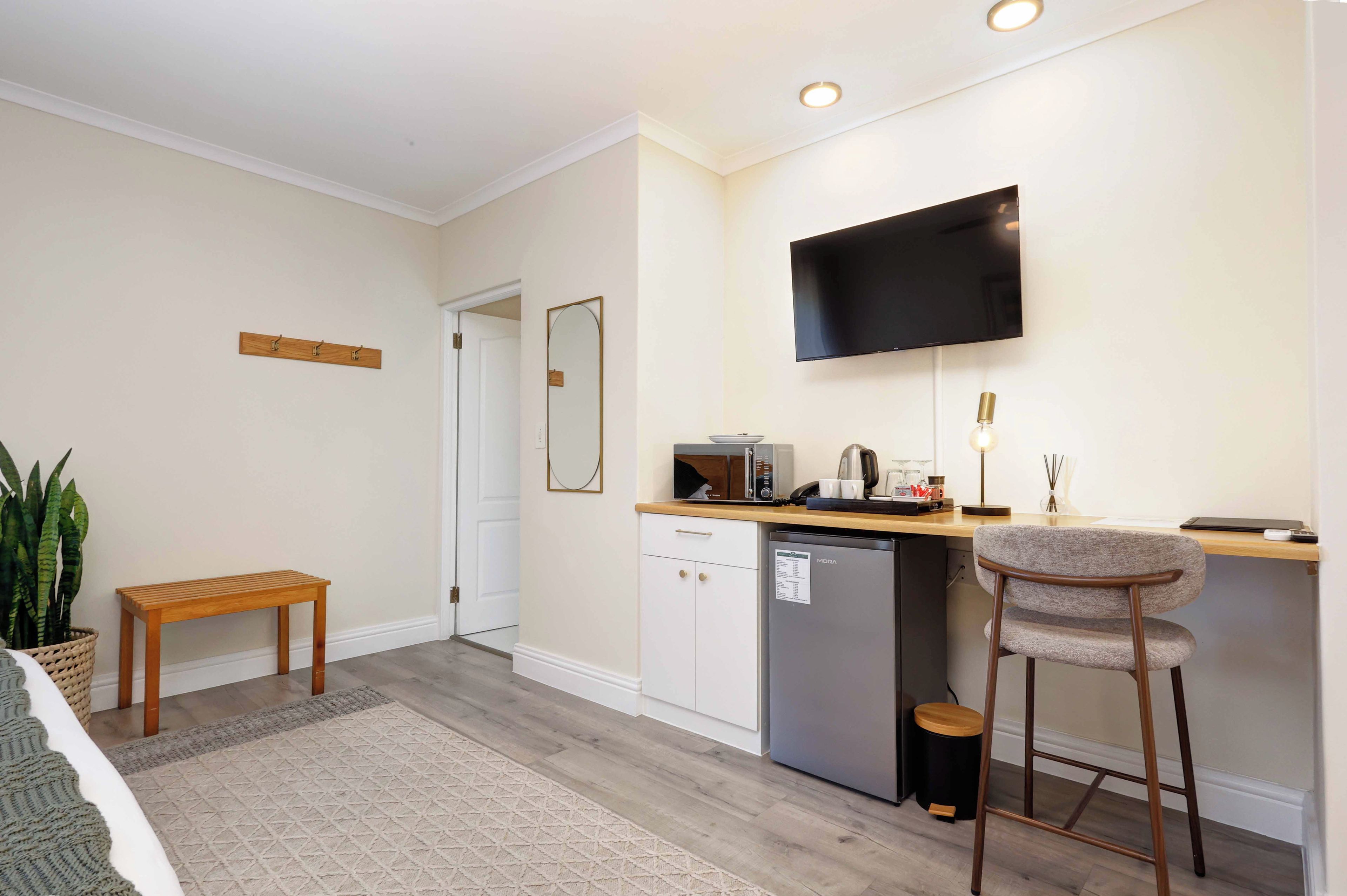 A compact kitchen with a built-in microwave, a refrigerator, a bar stool, and a flat-screen TV mounted on the wall.