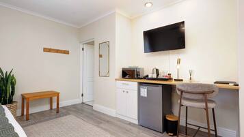 A compact kitchen with a built-in microwave, a refrigerator, a bar stool, and a flat-screen TV mounted on the wall.