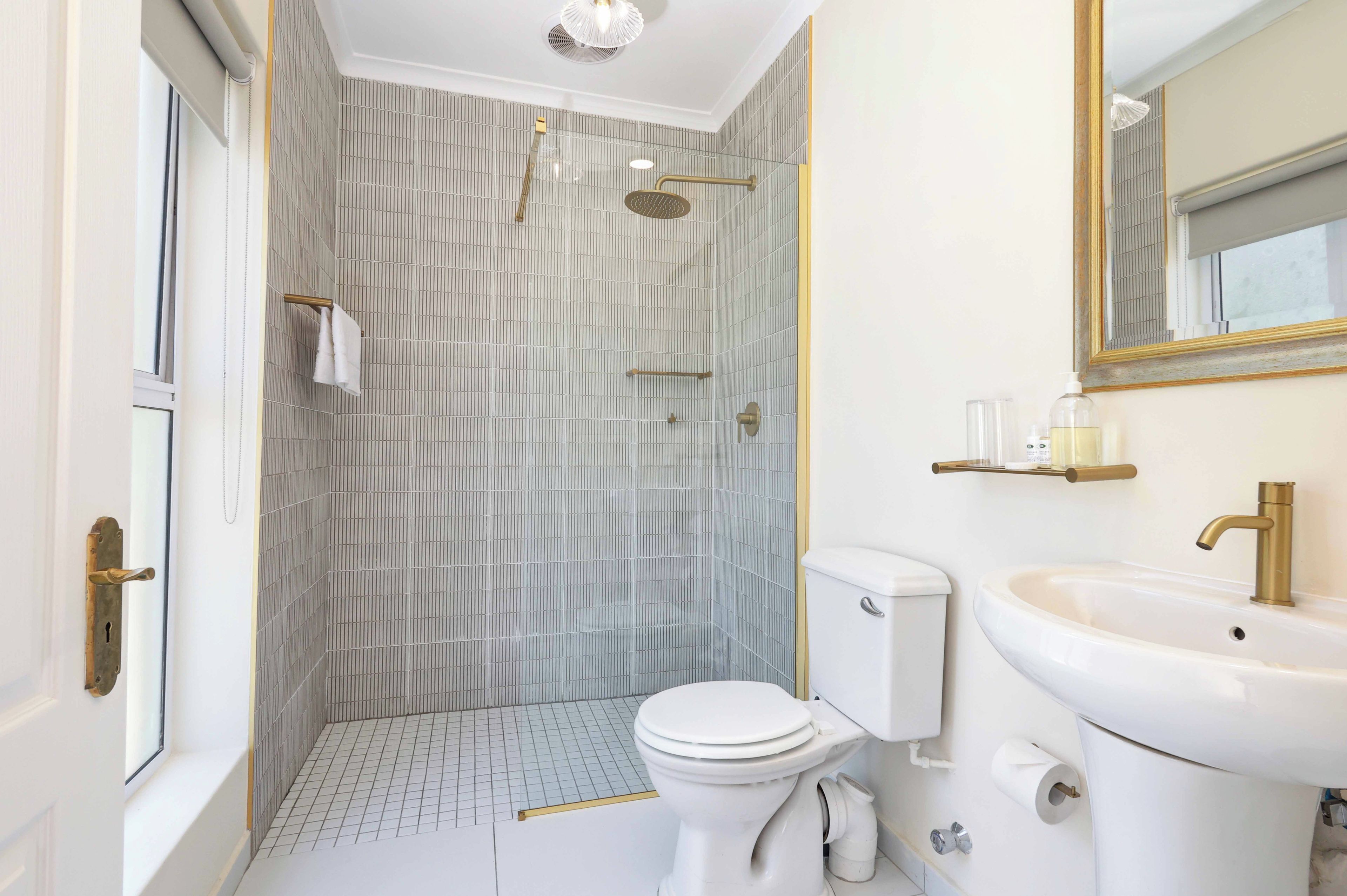A bathroom with a shower, toilet, sink, and mirror.