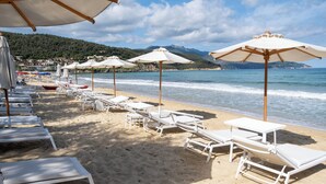 A beach with white sun loungers and umbrellas, a sandy shore, and a view of the sea and mountains in the background. - Baia Bianca Suites (Portoferraio)