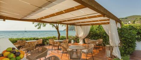 An outdoor patio with wooden flooring, wicker furniture, and a view of the sea.