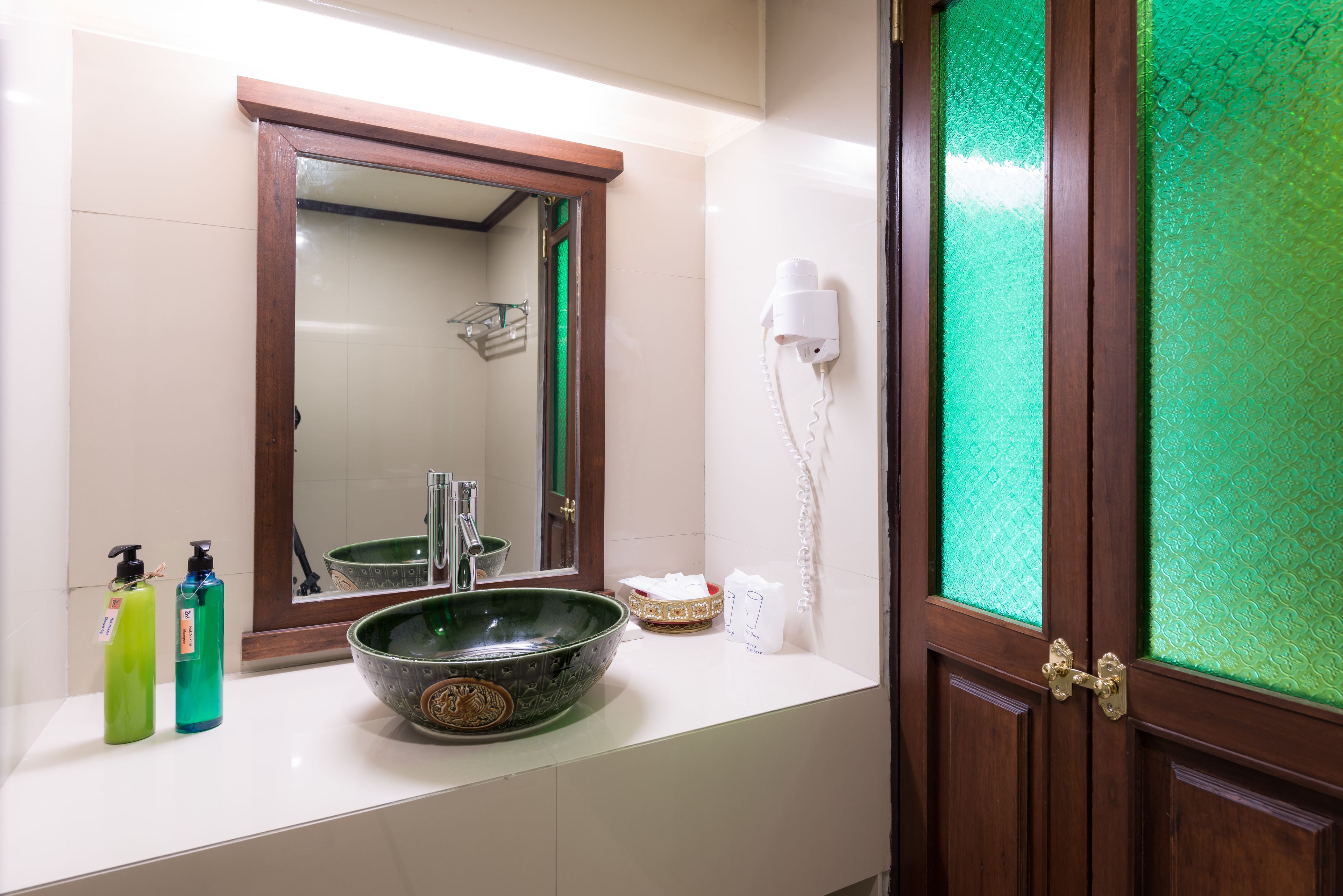 A bathroom with a large mirror, a green glass bowl sink, and toiletries on the counter.