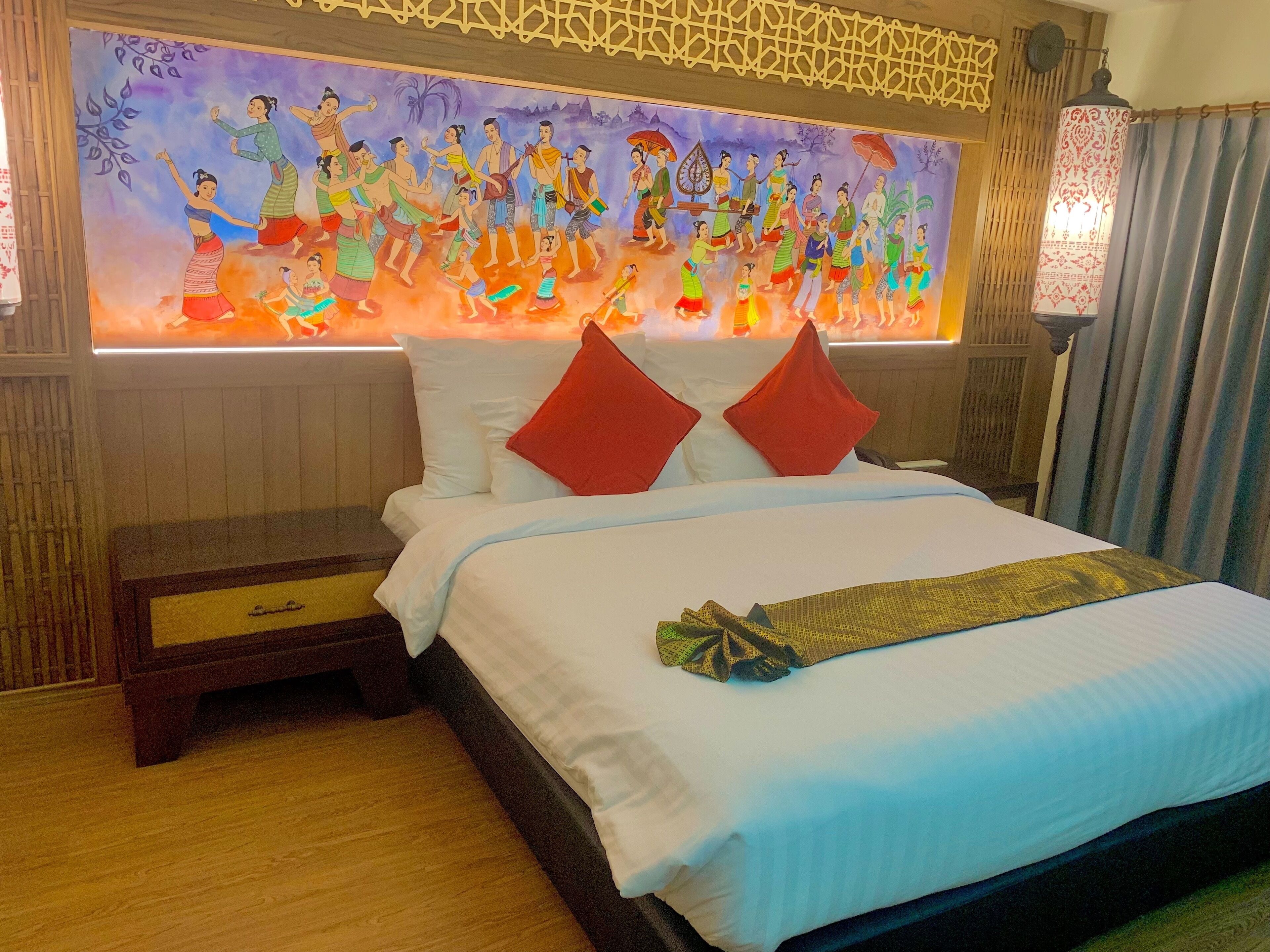 A hotel room with a bed, pillows, a nightstand, a lamp, and a wall mural.