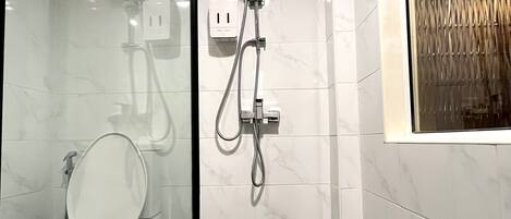 A bathroom with a toilet, a shower with a handheld showerhead, and a window with a curtain.
