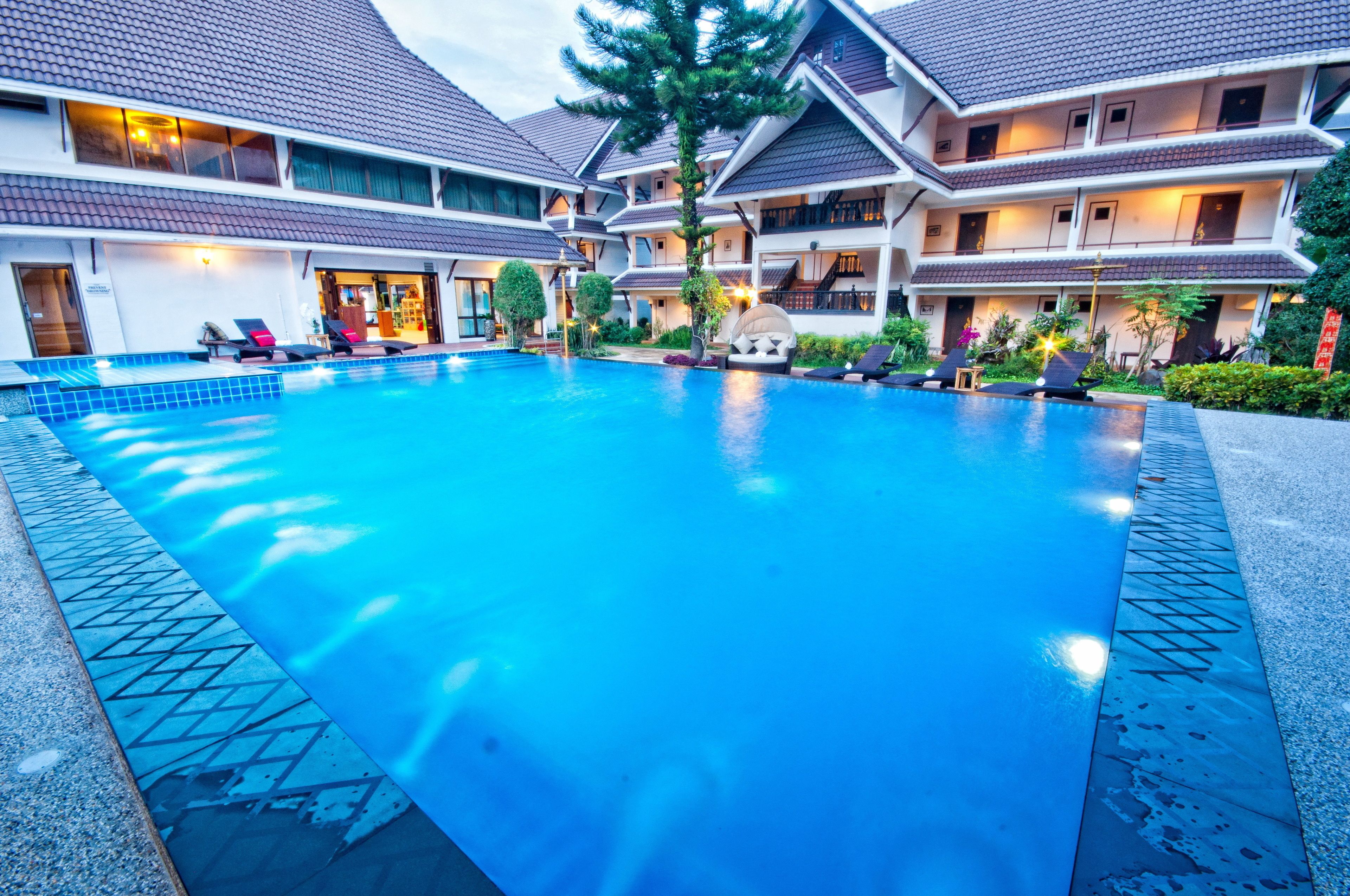 A hotel with a swimming pool, multiple balconies, and a well-maintained garden area.