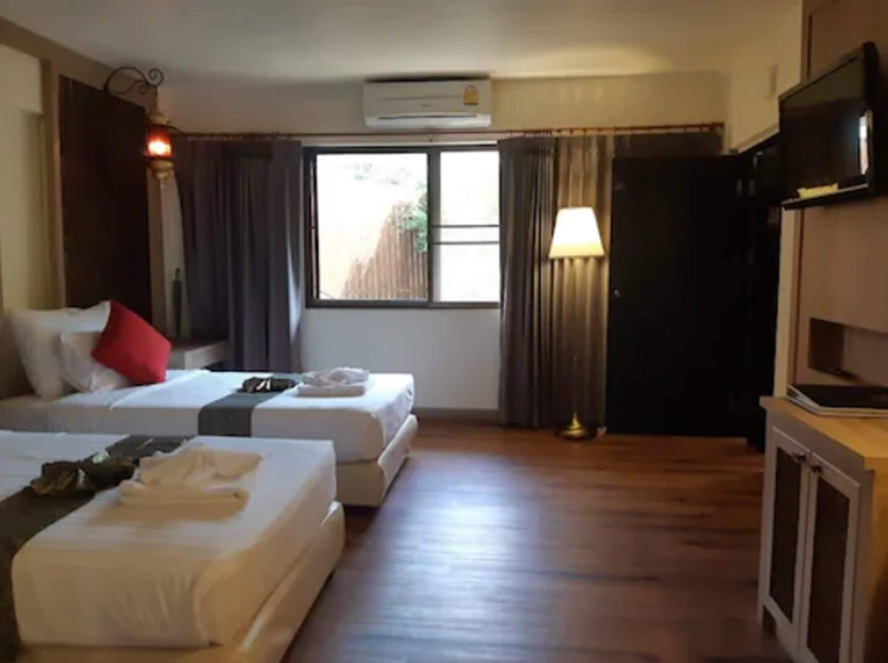 A hotel room with two beds, a TV, an air conditioner, and a window with curtains.