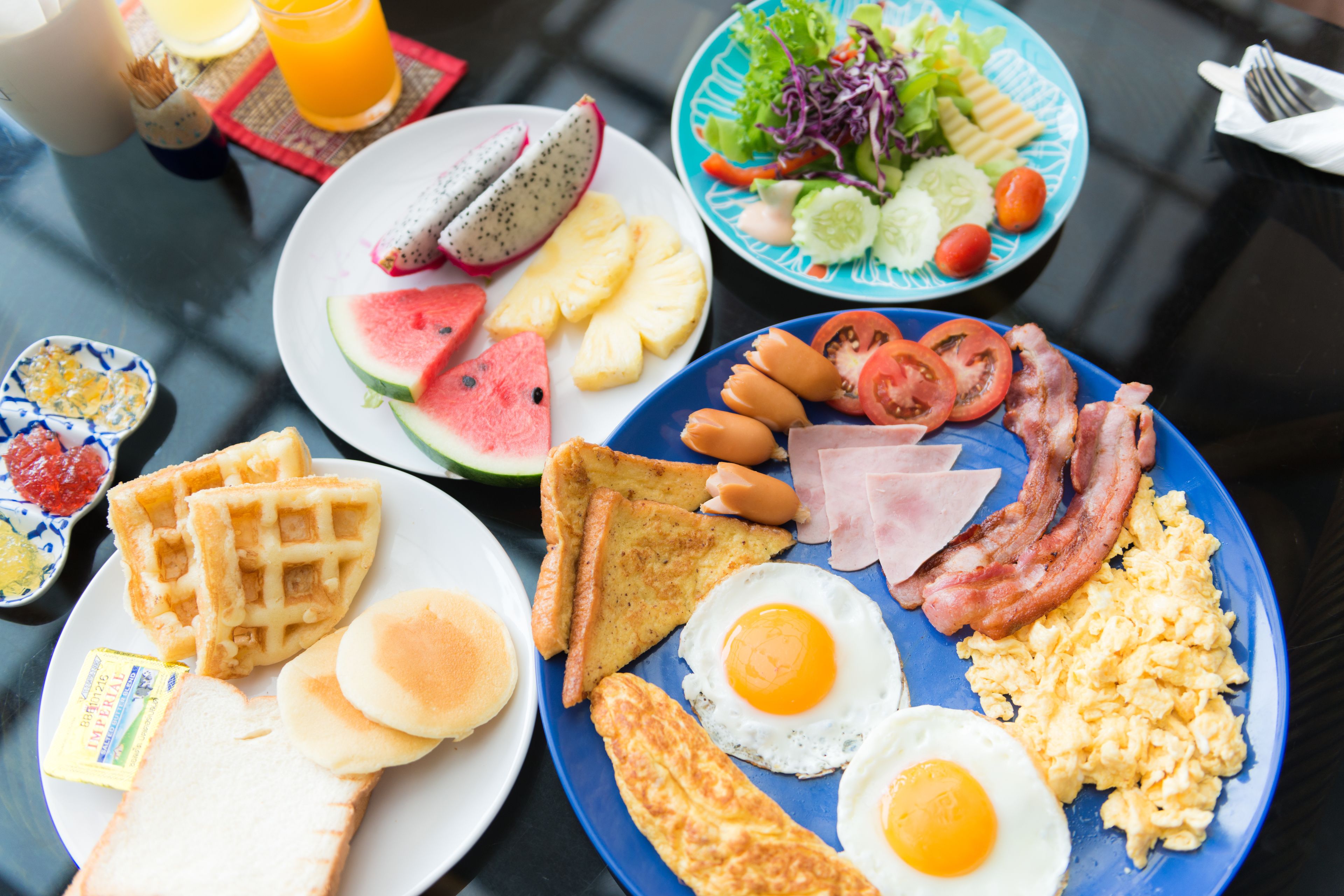 A breakfast spread with waffles, toast, eggs, bacon, and various fruits and vegetables.
