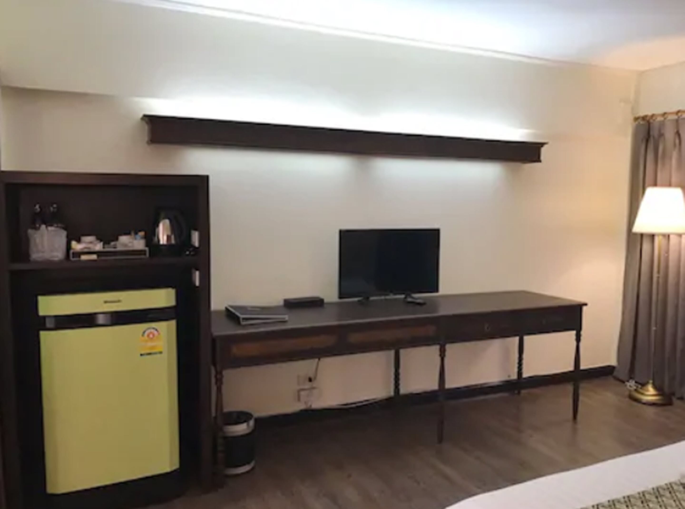 Une chambre d’hôtel équipée d’un bureau, d’une télévision, d’un mini-bar et d’une lampe.
