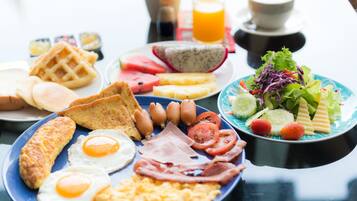Una abundante mesa de desayuno con huevos, tocino, salchichas, tostadas, gofres y una ensalada.