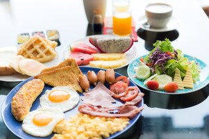 Una abundante mesa de desayuno con huevos, tocino, salchichas, tostadas, gofres y una ensalada.