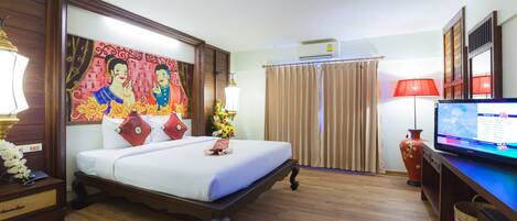 A hotel room with a bed, a television, a desk, a lamp, a vase, and a painting on the wall.