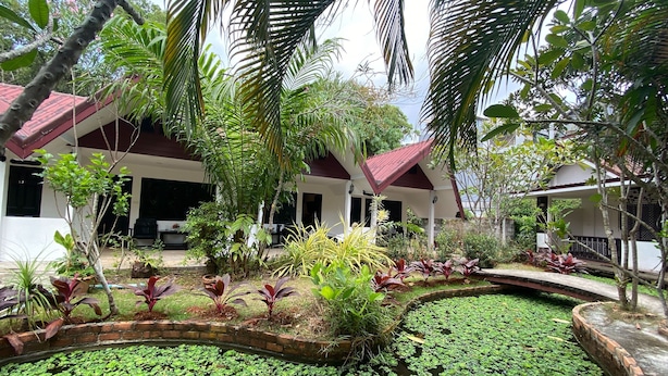 A house with a covered patio, surrounded by lush greenery and a pond with lily pads. - The Krabi Forest Homestay (Krabi)