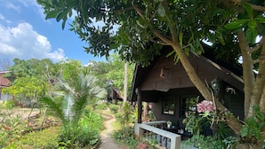 A rustic wooden house with a porch, surrounded by lush greenery and a gravel path. - The Krabi Forest Homestay (Krabi)