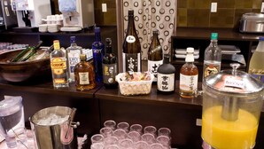 Un espace bar avec différentes bouteilles d’alcool, des verres et un grand récipient rempli de jus d’orange.