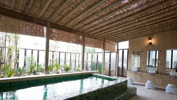 A swimming pool with a tiled edge, surrounded by a covered area with bamboo and plants. - Kuretake Inn Fujisan (Fuji)