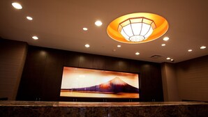 A lobby with a large wall-mounted TV displaying a mountain scene, recessed ceiling lighting, and a marble reception desk. - Kuretake Inn Fujisan (Fuji)
