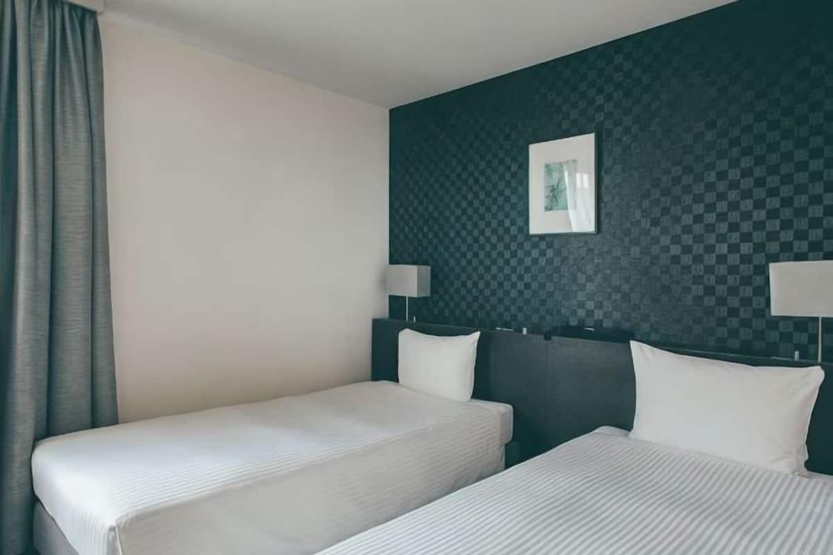 Une chambre dâhĂŽtel avec deux lits, un mur Ă motifs sombres et un tableau encadrĂ©.