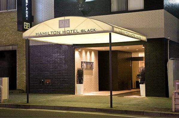 The exterior of the Hamilton Hotel Black, featuring a brick facade, a covered entrance with a sign, and potted plants.