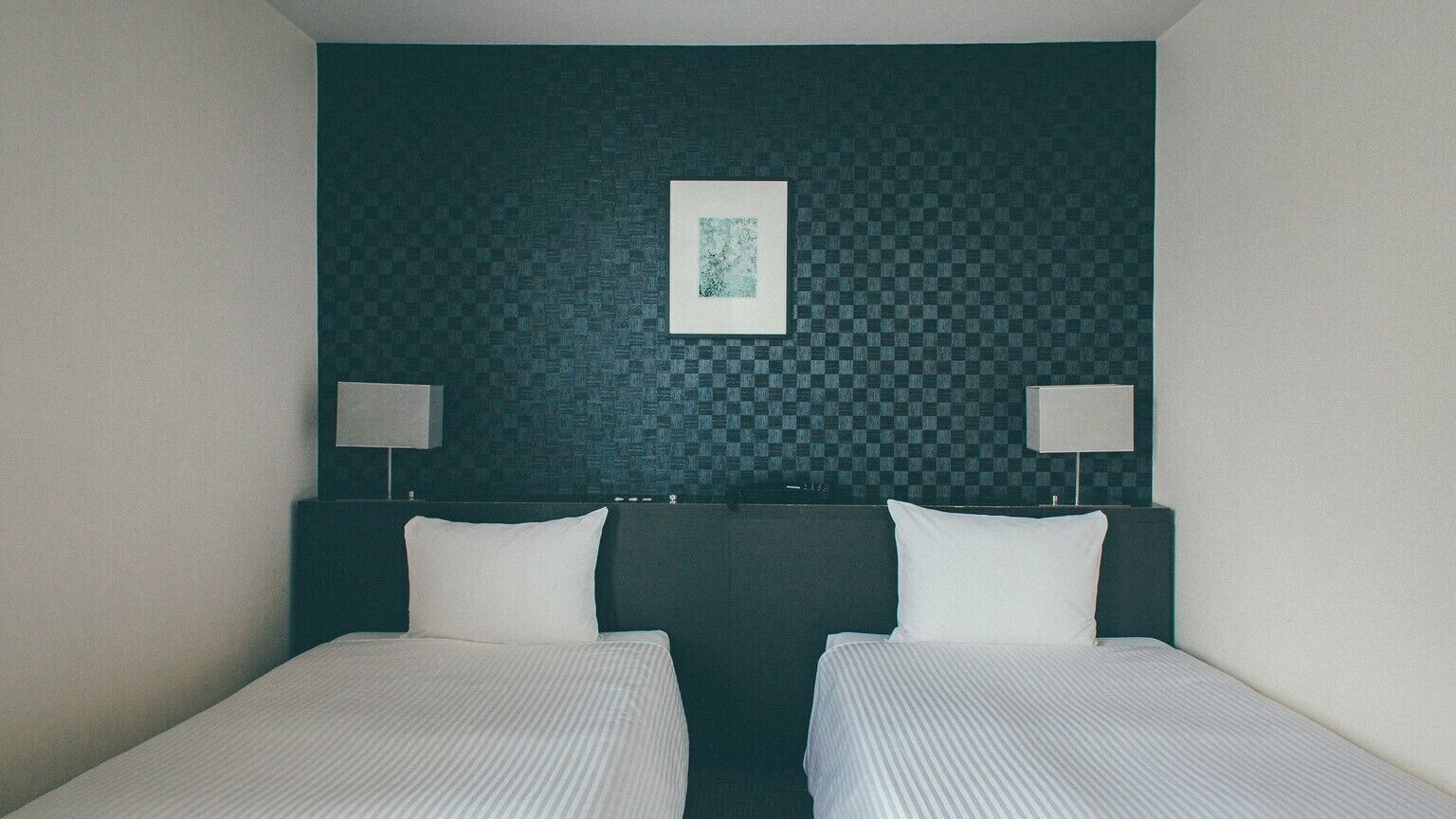 Ein Hotelzimmer mit einer karierten Wand, zwei Betten und zwei Nachttischlampen.