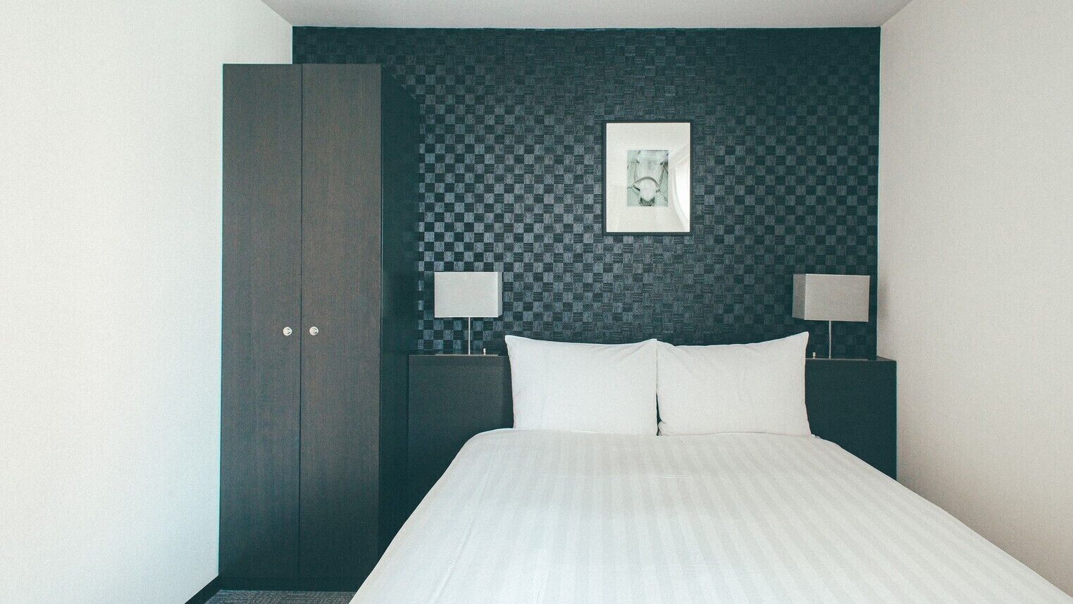 Ein Hotelzimmer mit Bett, Schrank, einer karierten Wand und zwei Nachttischlampen.