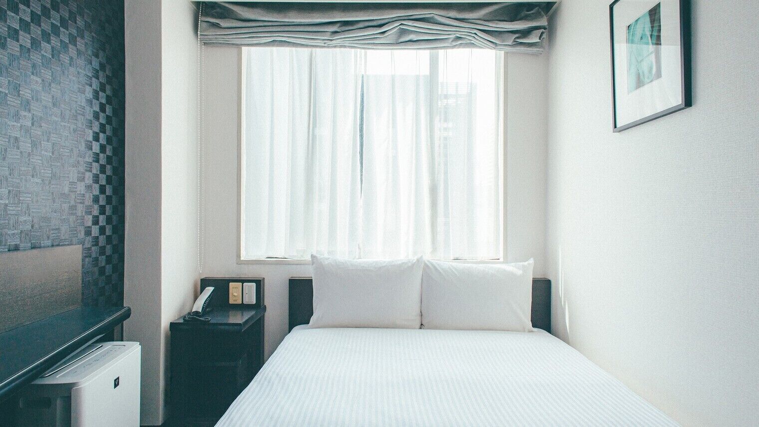 Ein Hotelzimmer mit Bett, Nachttisch, Schreibtisch, Heizung und einem fensterbepflanzten Fenster.