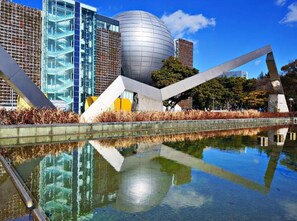 A modern building with a spherical structure and angular sculptures in front of a reflective water body.